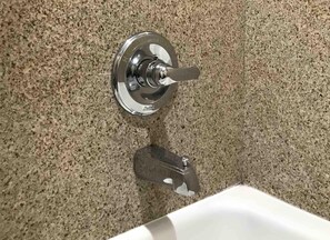 A bathroom with a granite countertop, a chrome faucet, and a white bathtub.