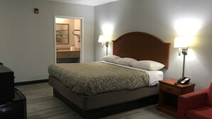 A hotel room with a bed, bedside lamps, a telephone, a red chair, and a desk.