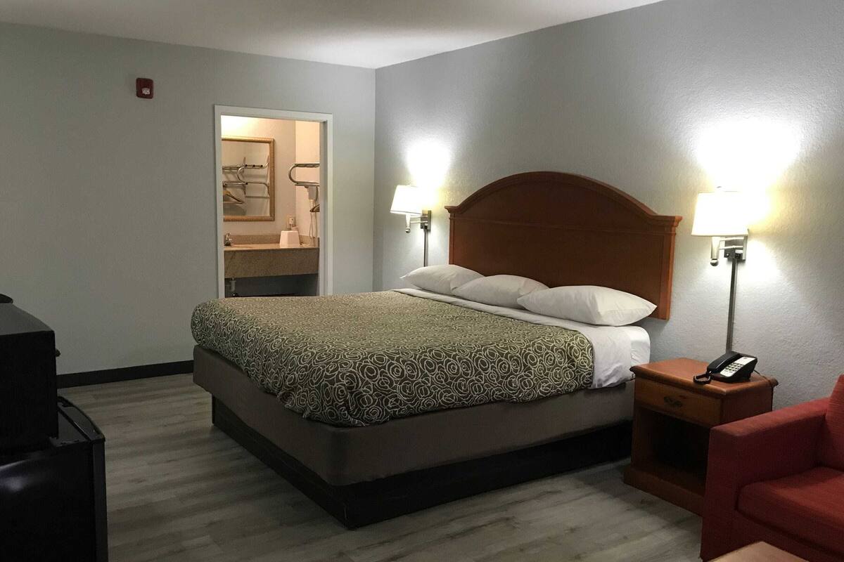 A hotel room with a bed, bedside lamps, a telephone, a red chair, and a mirror.