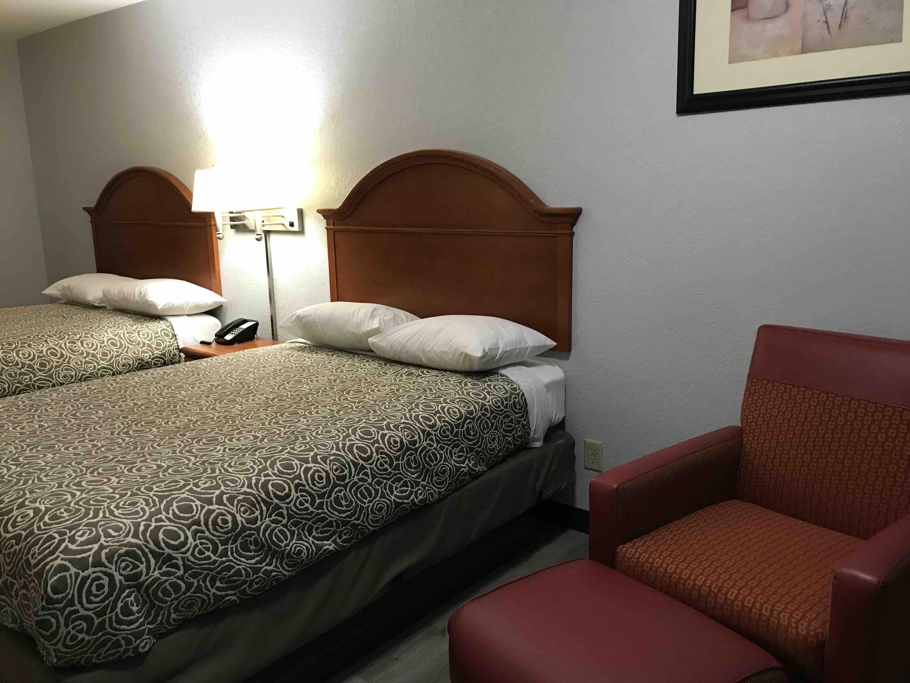 A hotel room with two beds, a red armchair, and a bedside table with a lamp.