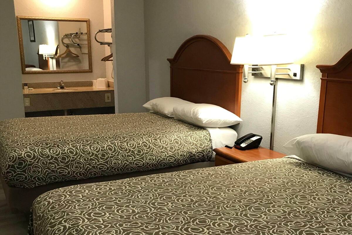 A hotel room with two beds, a bathroom with a mirror, and a bedside lamp.