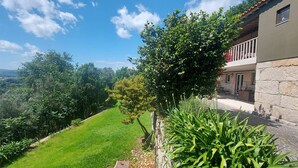 A hillside property with a stone building, lush greenery, and a clear view of the surrounding landscape. - Casas da Tapada - Casa das Cortes (Guimarães)