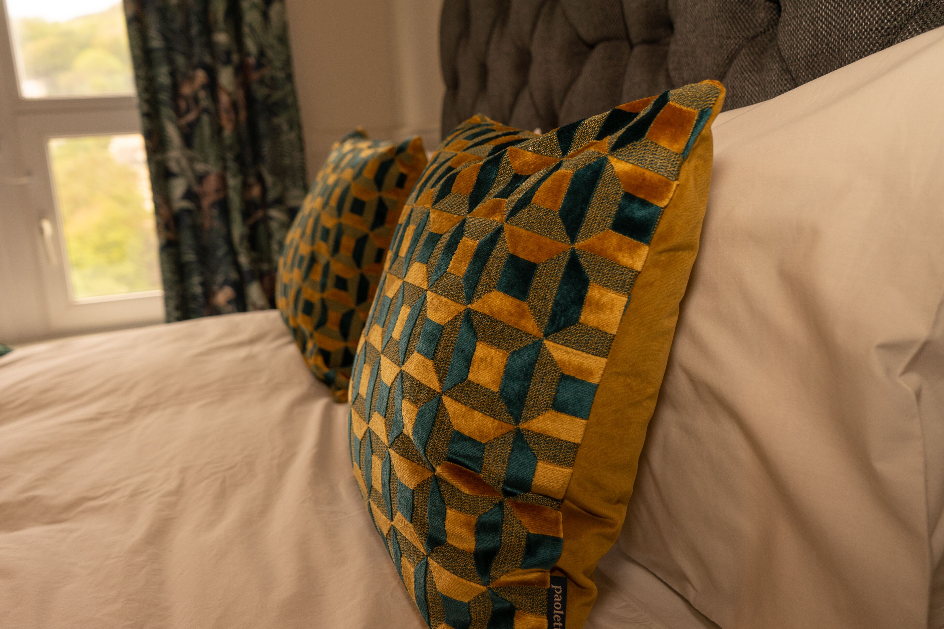 Un lit avec des coussins à motifs et une fenêtre avec des rideaux.