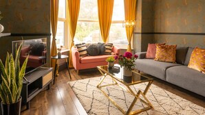 Una sala de estar con sofá, sillón y mesa de centro. Hay un televisor y una planta.