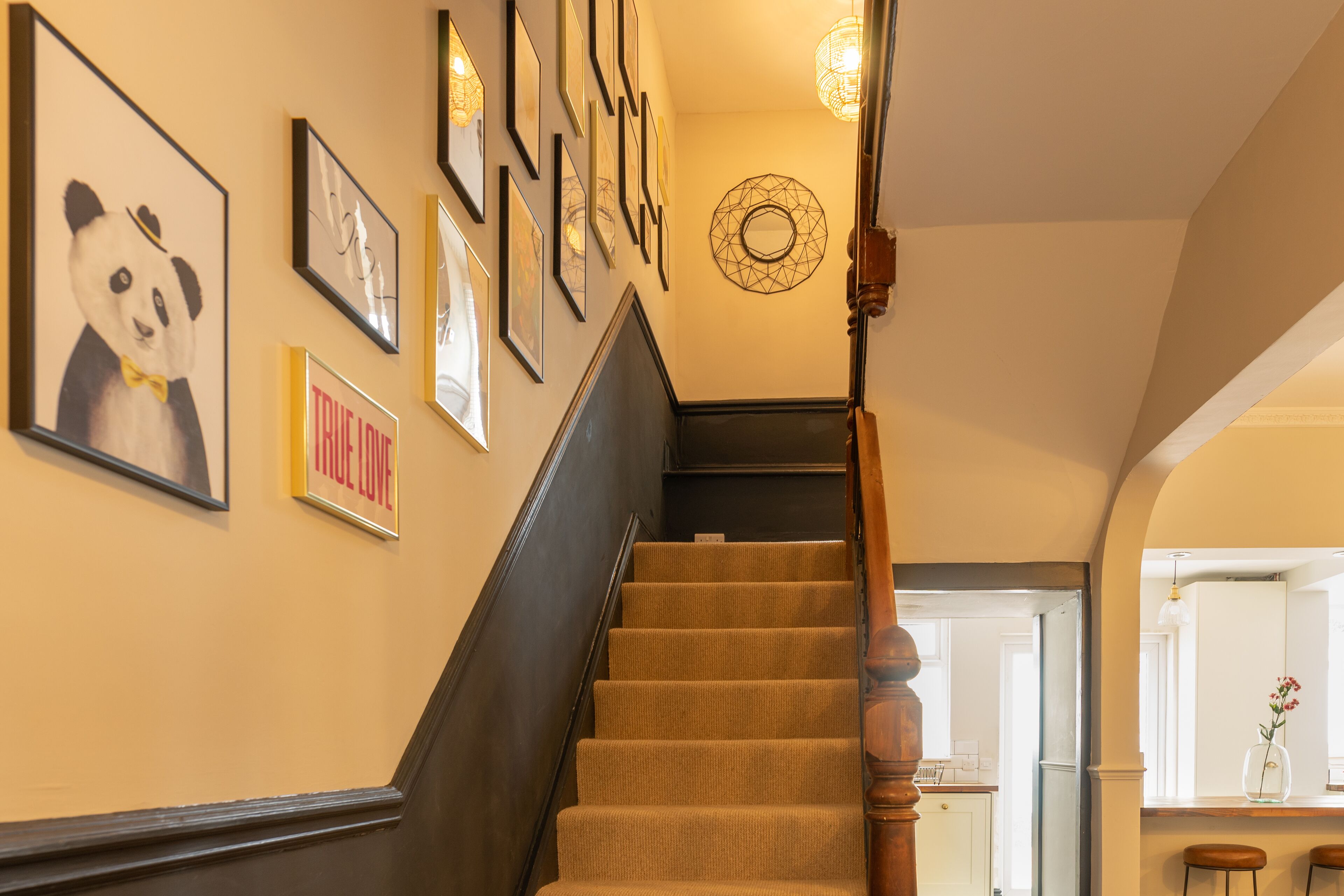 A staircase with a wooden handrail, beige carpeted steps, and framed artwork on the walls.