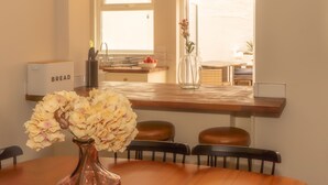 Un comedor con una mesa de madera, sillas, un florero con flores y una cocina al fondo.