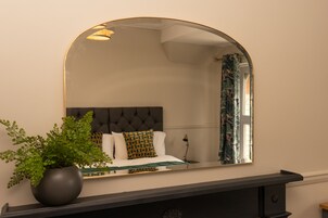 Un dormitorio con cama, planta en maceta, espejo y mesita de noche.