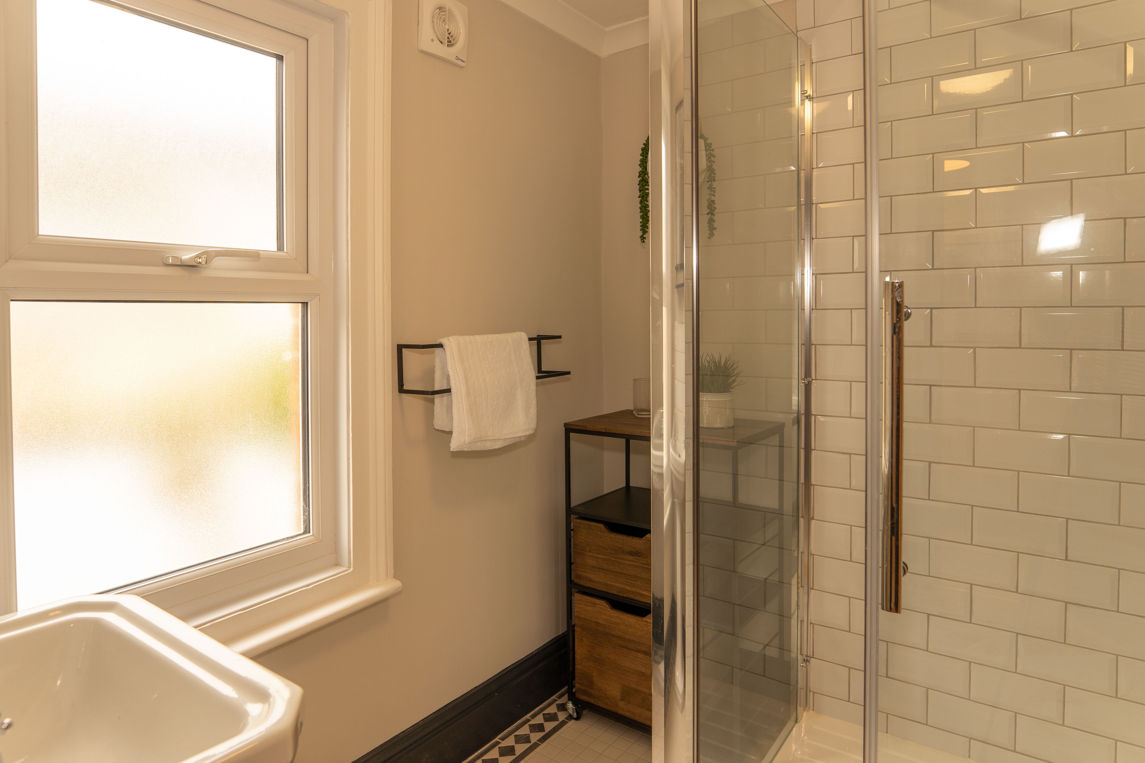 A bathroom with a glass-enclosed shower, a white sink, and a window.