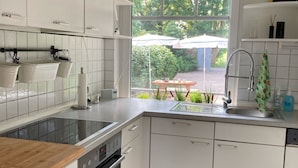 Una cocina moderna con armarios blancos, un lavamanos de acero inoxidable y una ventana con vistas a un jardín.