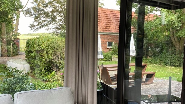 Una sala moderna con un sofá, un ventanal de vidrio que da a un patio y vistas a un jardín y un edificio.