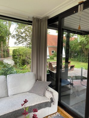 Una sala moderna con un sofá, un ventanal de vidrio que da a un patio y vistas a un jardín y un edificio.