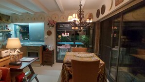 Una zona de menjador acollidora amb una taula preparada per a dues persones, un penjoll i vista a un patí exterior a través d'una porta de vidre.