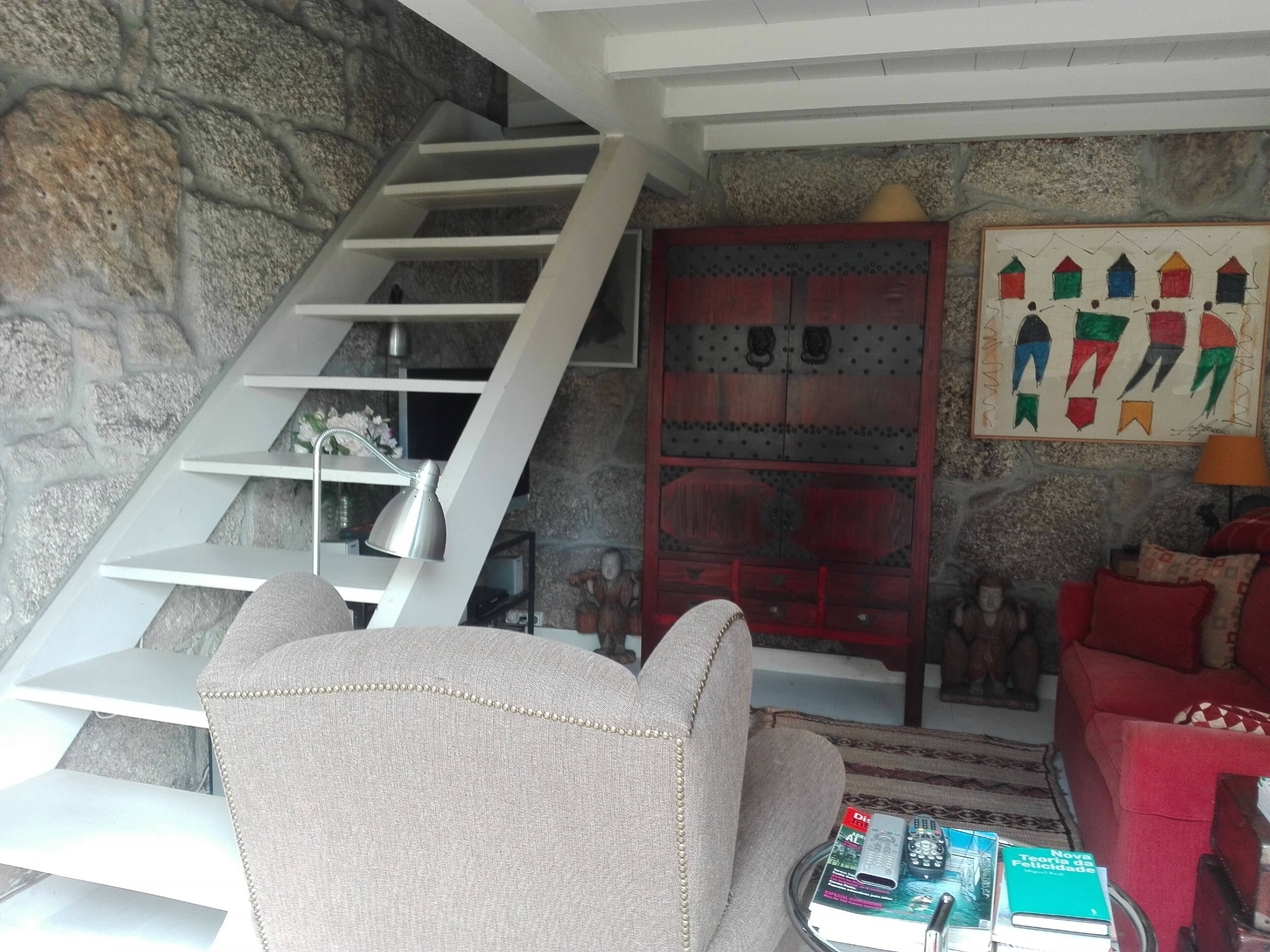 Un salon avec un mur en pierre, un escalier, un meuble rouge et un canapé rouge.
