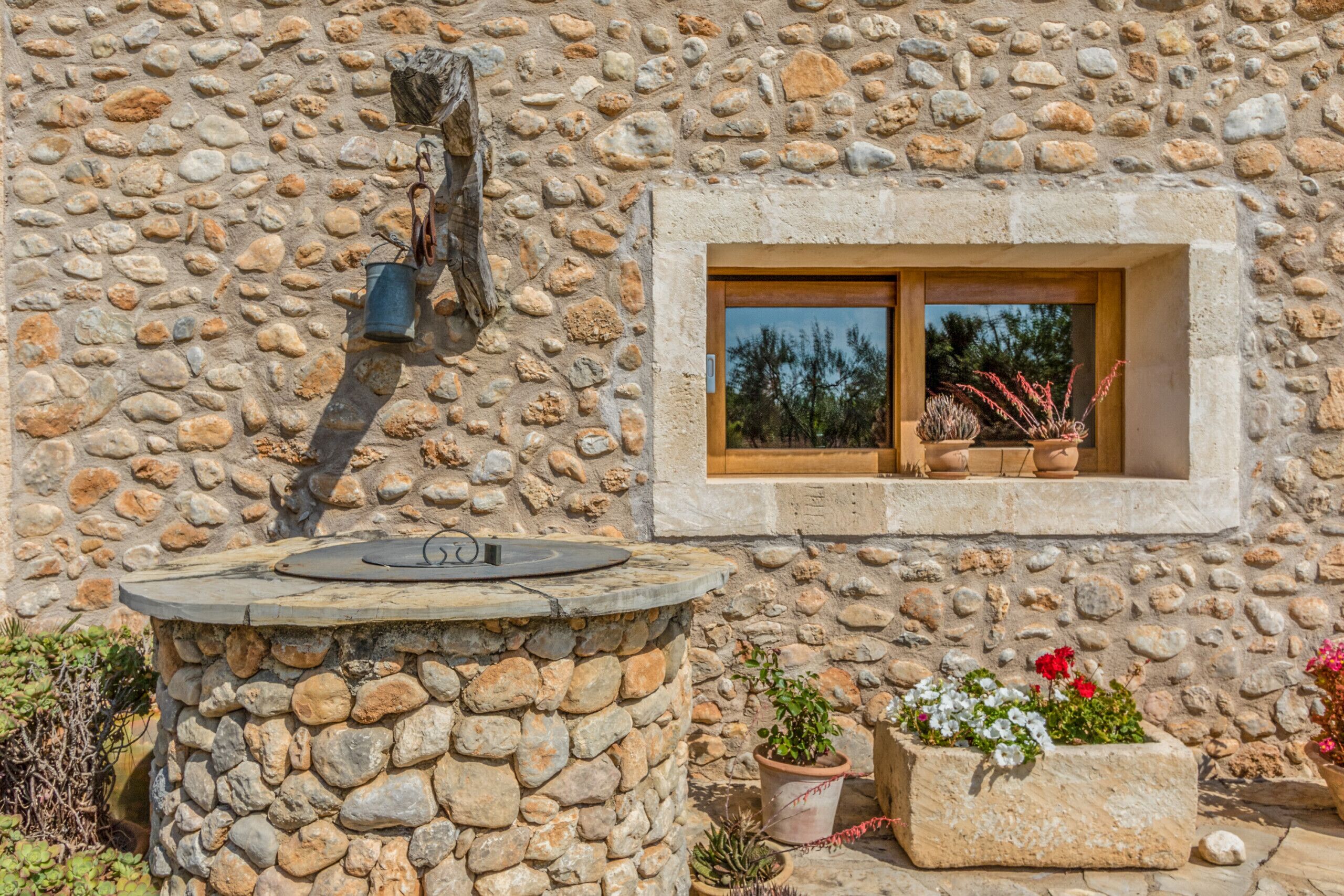 A stone wall with a window, a stone fountain, and potted plants.