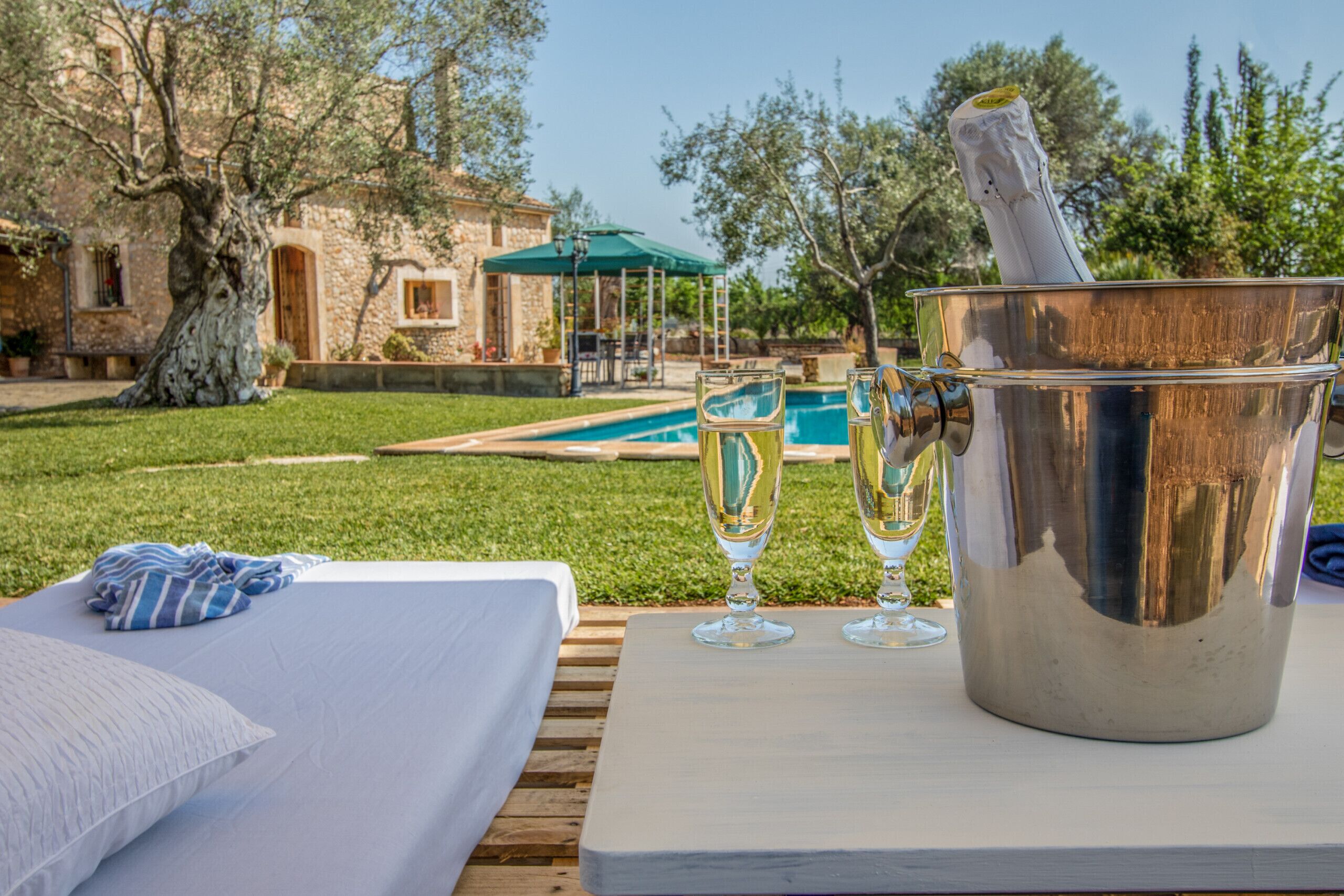 A poolside setting with a bed, a bucket with a champagne bottle, and two glasses.