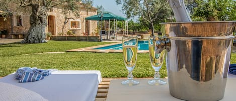 A poolside setting with a bed, a bucket with a champagne bottle, and two glasses.