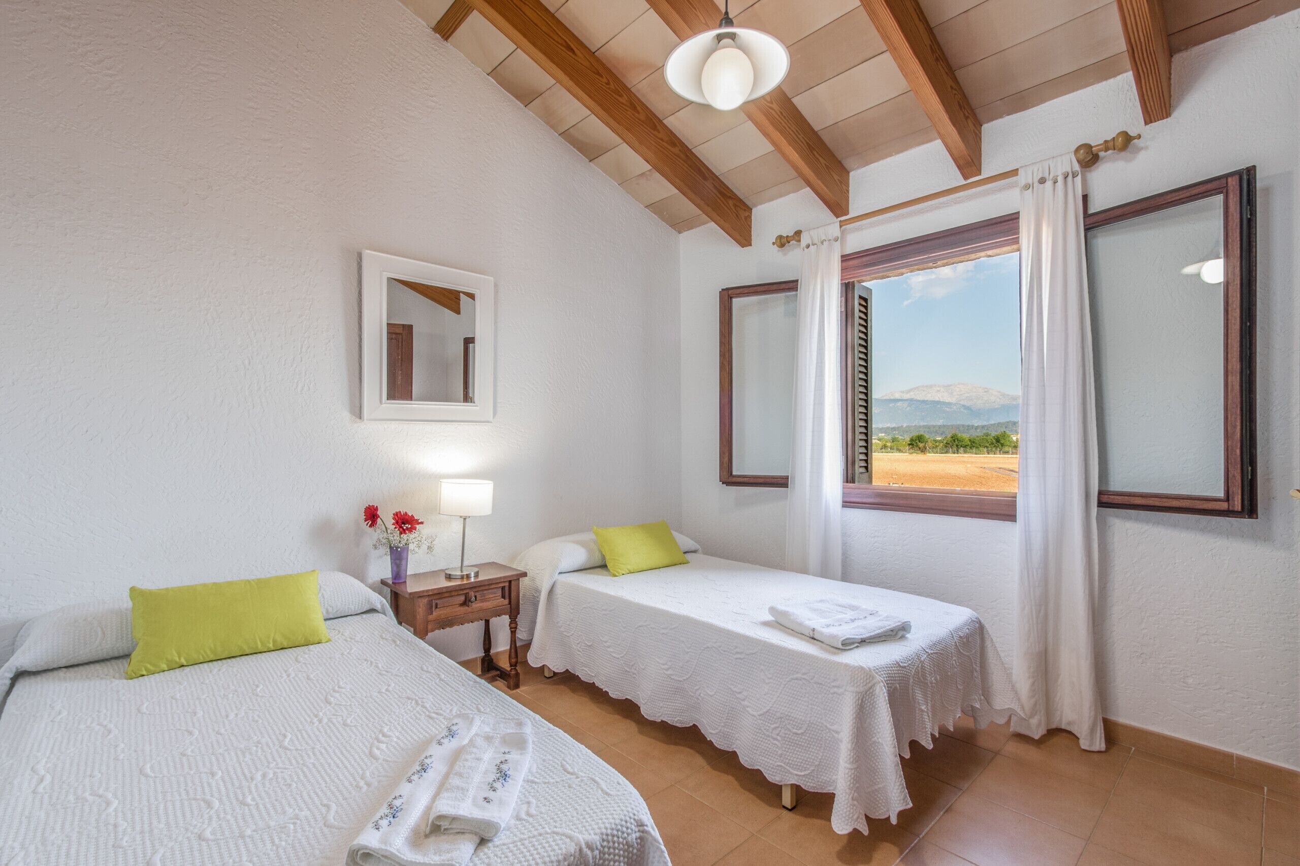 A bedroom with two beds, a nightstand, a lamp, and a window with curtains.