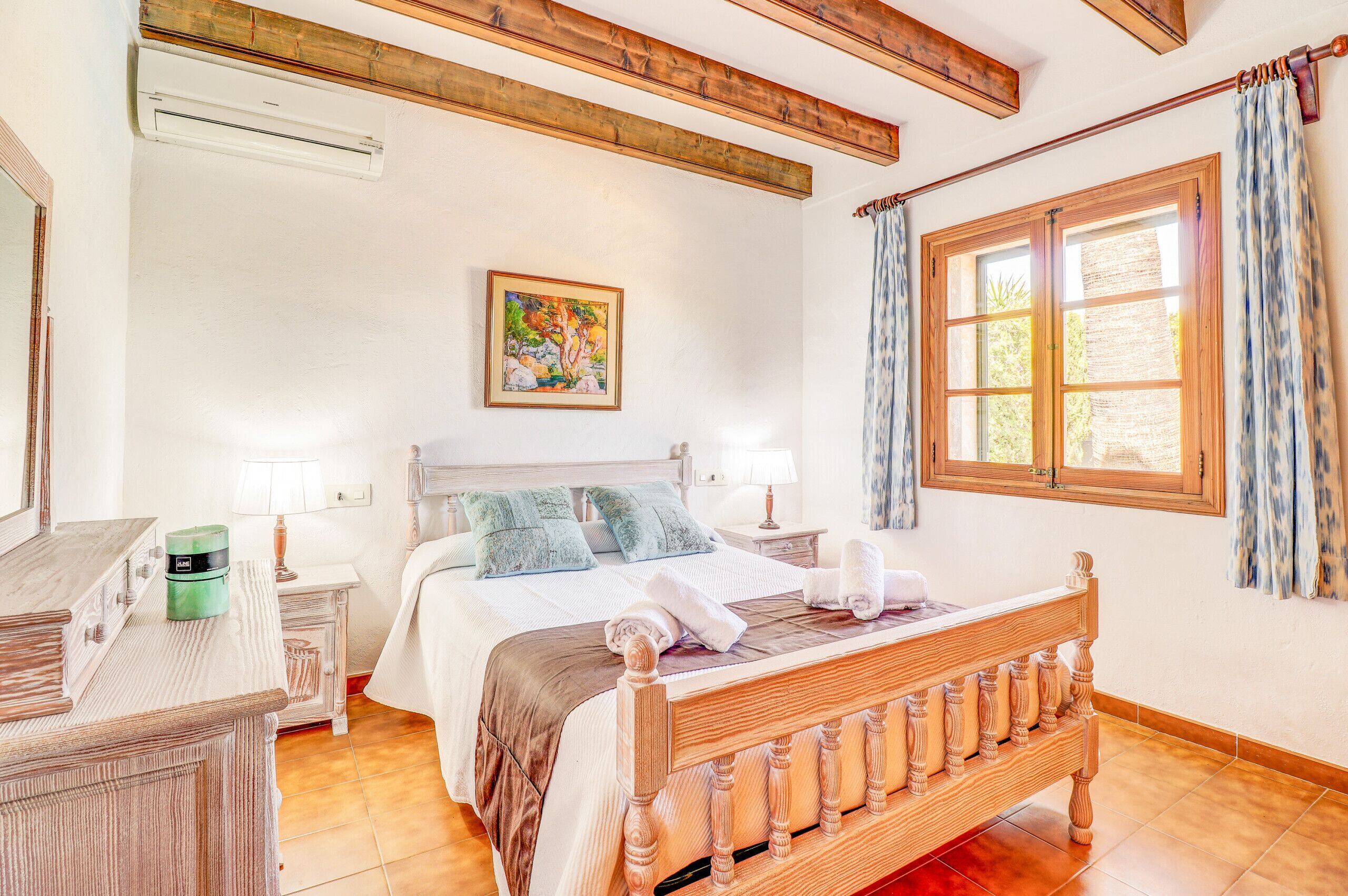 Une chambre à coucher avec un lit en bois, une table de chevet, une commode, un tableau au mur et une fenêtre avec des rideaux.