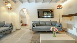 Een moderne woonkamer met een grijze bank, een salontafel met een bloevas, en een flatscreen televisie aan de muur.