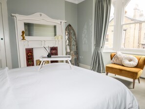 A bedroom with a large bed, a small table, a chair, and a window with curtains. - 39 West Street (Scarborough)