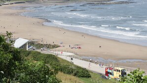 A coastal beach with a sandy shore, a promenade, and a bus in the foreground.