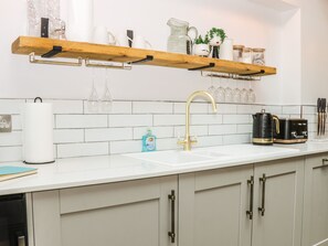 A kitchen with a white countertop, a gold faucet, and a wooden shelf above the sink. - 39 West Street (Scarborough)