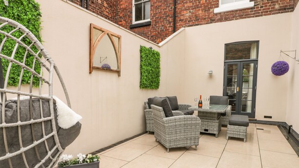 A patio with wicker furniture, a hanging chair, and a small table with a bottle and glasses.