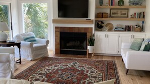 Ein großzügiges Wohnzimmer mit Kamin, weißen Sofas, einem großen Fernseher und einem Deckenventilator.