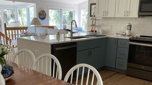 Eine moderne Küche mit weißen Schränken, einem eingebauten Backofen und einem Essbereich mit einem Holztisch und weißen Stühlen.