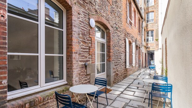 A narrow outdoor patio with stone flooring and blue metal chairs and tables. - La Cour des Carmélites 2 - Studio calme en centre-ville (Rennes)