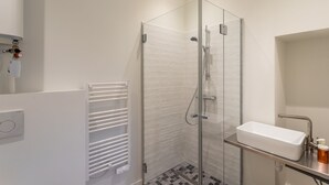 A modern bathroom with a glass shower enclosure, a white sink, and a towel rack. - La Cour des Carmélites 2 - Studio calme en centre-ville (Rennes)