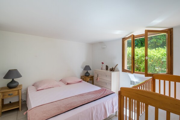 A bedroom with a bed, bedside tables, a dresser, and a window with a view of greenery.
