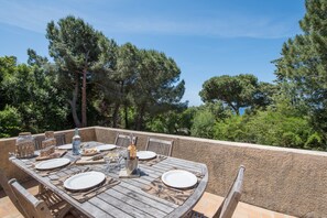 An outdoor dining area with a rustic wooden table set for four, surrounded by chairs.