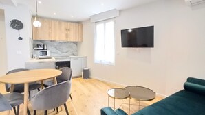 A compact living space with a dining area, kitchenette, and a flat-screen TV mounted on the wall. - Viva Riviera Palais Holiday Design 2 Bedrooms (Cannes)