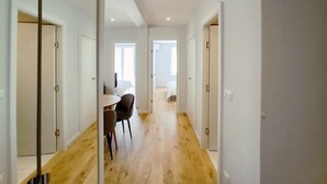 A corridor with wooden flooring, white walls, and doors leading to bedrooms. There is a dining area with a table and chairs. - Viva Riviera Palais Holiday Design 2 Bedrooms (Cannes)