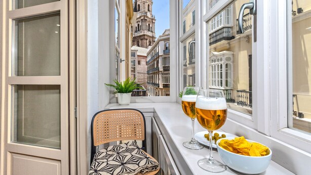 A balcony with a view of a historic building, two glasses of beer, a bowl of chips, and a wicker chair. - Wonderful 1-bedroom apartment in Malaga center. San Agustin I (Malaga)