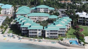 A resort with multiple buildings featuring a consistent architectural style, a beachfront, and a swimming pool area. - Beach Living at Plantation Village BLGS (Seven Mile Beach)