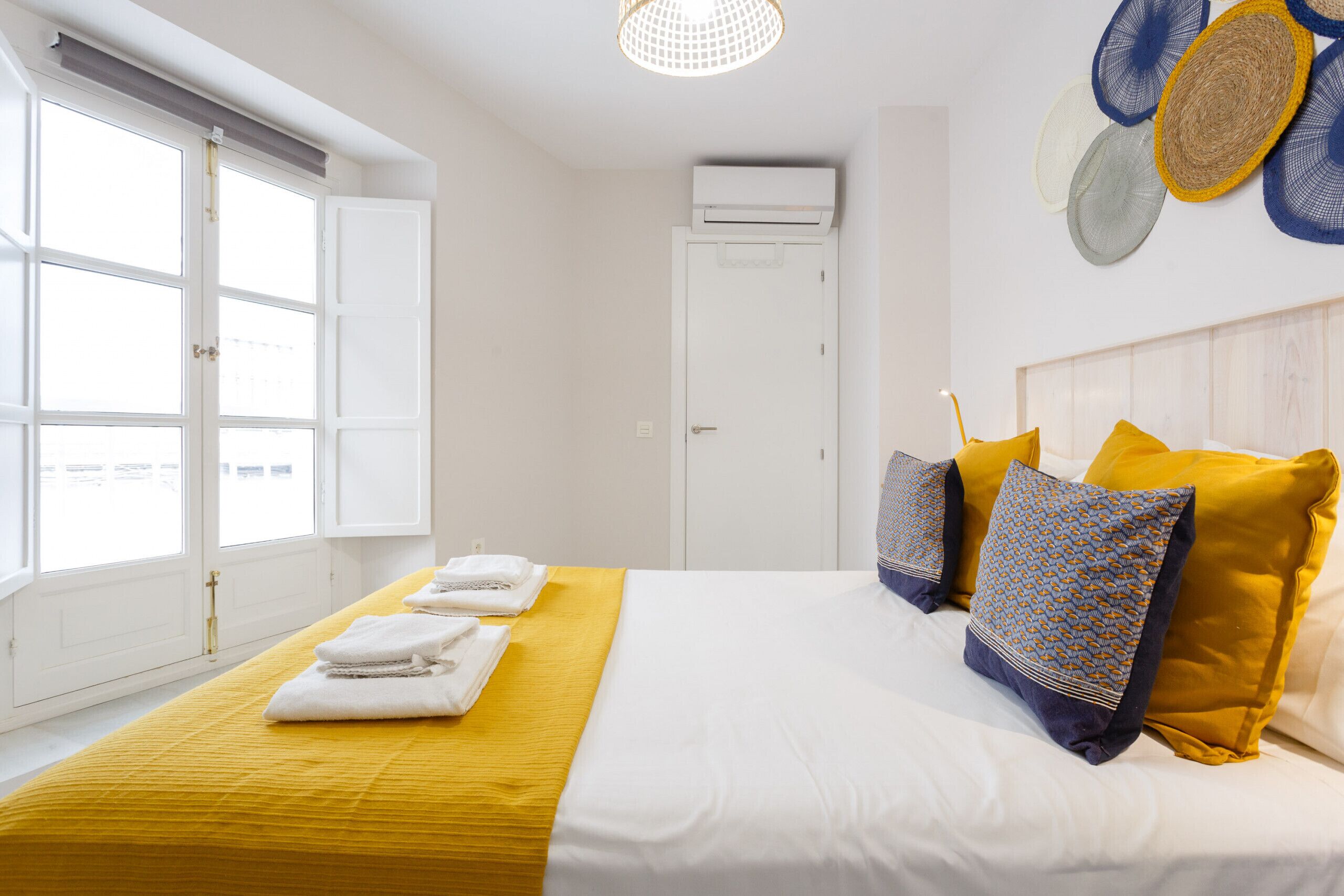 A hotel room with a bed, white walls, a window, and a door.