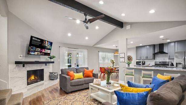 A modern living room with a fireplace, grey sofa, colorful cushions, and a flat-screen TV mounted on the wall.