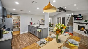 A modern kitchen with a central island, a dining area with a table set for two, and a living area with a fireplace and a TV.