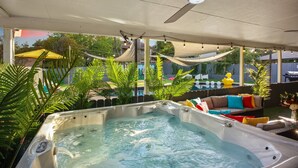 A hot tub area with a ceiling fan, surrounded by potted plants and a pool in the background.
