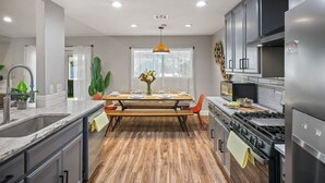 A modern kitchen with a wooden dining table, stainless steel appliances, and a large window.