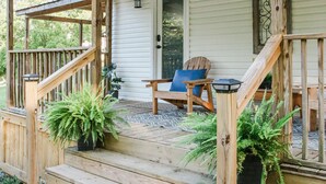 A wooden porch with a set of stairs leading to a door, a chair, and a table. - Moonlight Cottage - Romantic Smoky Mountain Cabin with Hot Tub & Community Pool (Sevierville)