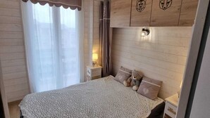 A bedroom with a large bed, a nightstand, a wall-mounted light, and a window with curtains. - 45 m2 FULLY RENOVATED APARTMENT IN THE HEART OF THE ANGLES 4/6 BEDROOMS (Les Angles)