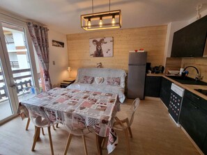 A cozy bedroom with a bed, a small table, and chairs. There is a kitchen area with a refrigerator and a sink.