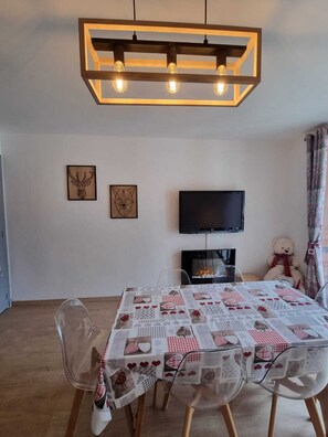 A dining area with a table covered in a patchwork quilt, clear chairs, and a modern pendant light fixture.