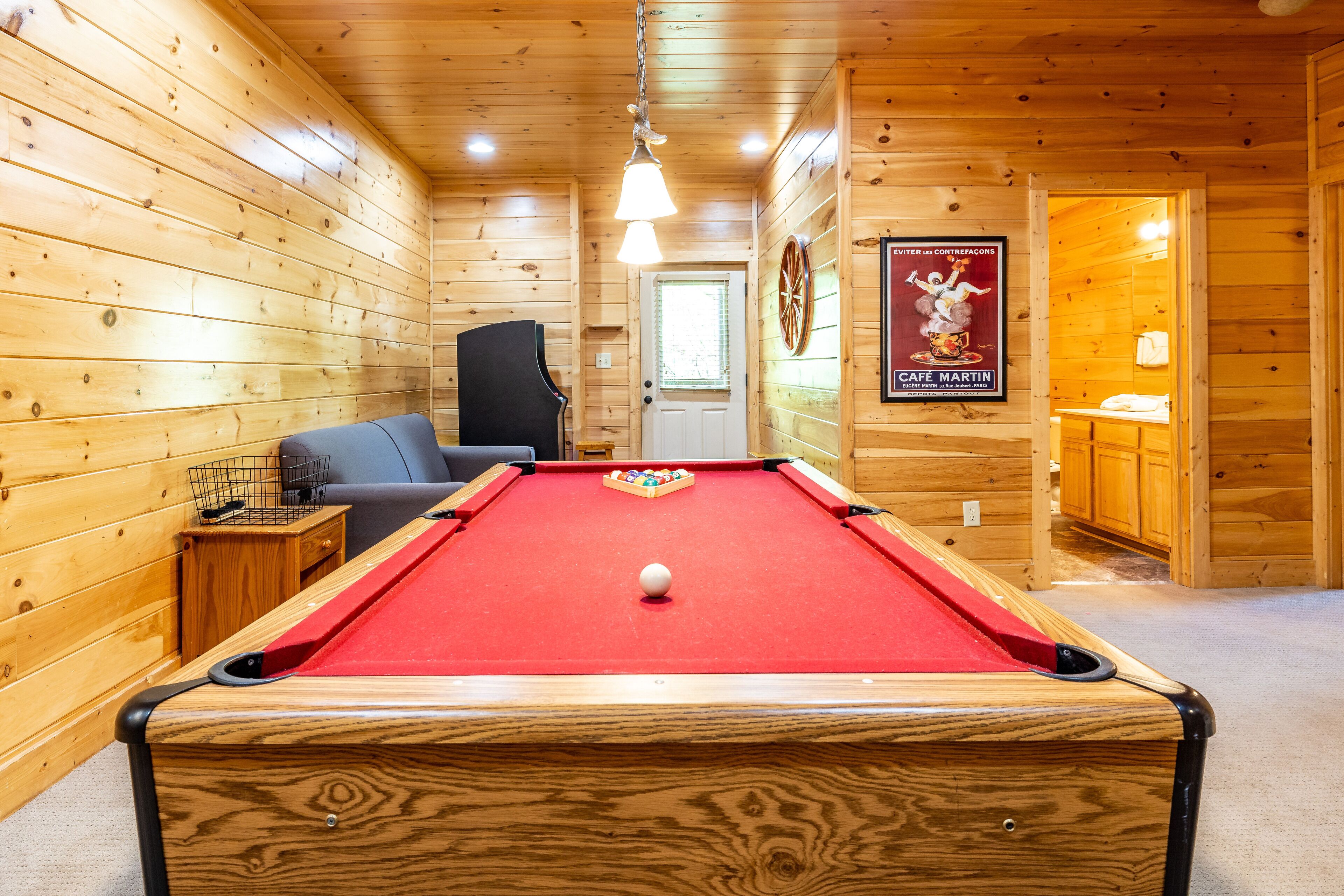 A pool table in a wooden room with a door, a chair, and a poster on the wall.