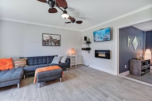 Una sala de estar con un sofá modular, una chimenea, un ventilador de techo y un televisor montado en la pared.