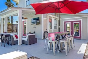 Un patio al aire libre con una mesa, sillas y un paraguas rojo.