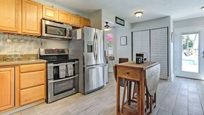 Une cuisine avec des meubles en bois, des appareils en acier inoxydable, un tabouret de bar en bois et une vue sur l’extérieur.
